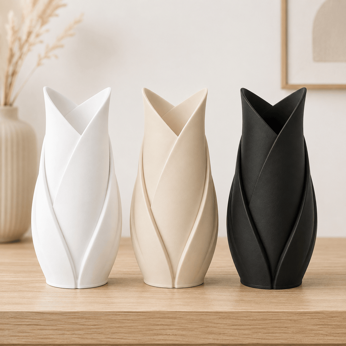 Three modern 3D printed tulip-shaped vases in white, beige, and black, arranged on a light wood surface against a soft neutral background.